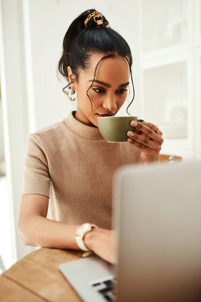 Кава і технології рухаються в руці. приваблива молода бізнес-леді сидить і насолоджується чашкою кави, використовуючи свій ноутбук вдома
 - Фото, зображення