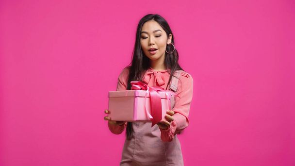 amazed young asian woman holding wrapped present isolated on pink  - Fotó, kép