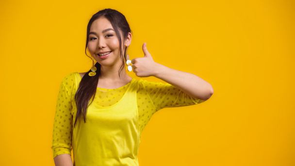 happy asian woman showing thumb up and smiling isolated on yellow  - Фото, изображение