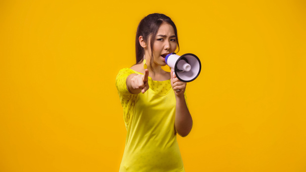 Hoşnutsuz Asyalı kadın megafonla bağırıyor ve sarıya izole edilmiş bir parmakla işaret ediyor.  - Fotoğraf, Görsel
