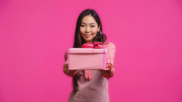 complacido joven asiático mujer holding envuelto presente aislado en rosa  - Foto, imagen