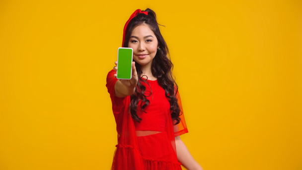 黄色で隔絶された緑の画面のスマートフォンを持っている陽気なアジアの女性  - 写真・画像