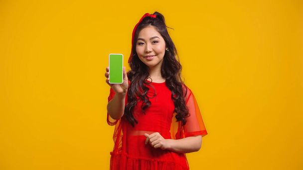 happy asian woman holding smartphone with green screen isolated on yellow  - Foto, imagen