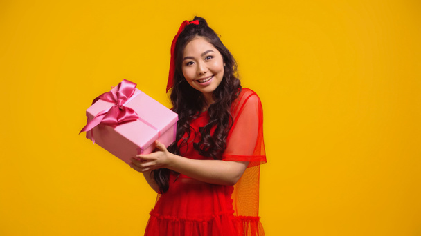 glückliche junge asiatische Frau hält verpacktes Geschenk isoliert auf gelb  - Foto, Bild