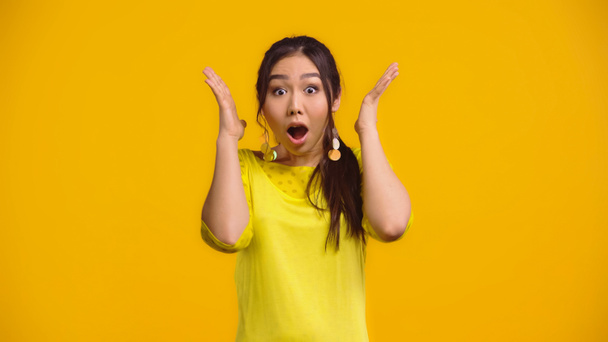 шокированная азиатка с открытым ртом, жестикулирующая изолированной на желтом   - Фото, изображение