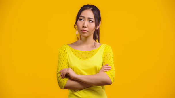 preoccupato e giovane donna asiatica in piedi con le braccia incrociate isolato su giallo  - Foto, immagini