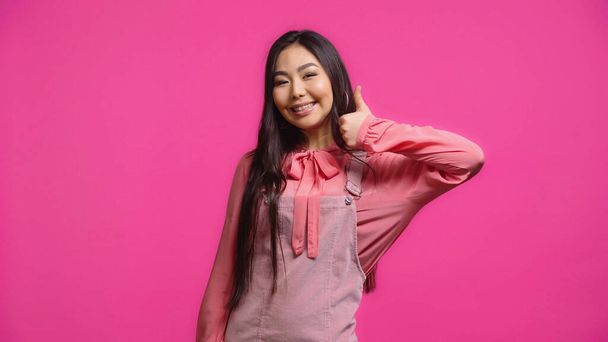 happy and brunette asian woman showing thumb up isolated on pink - Photo, Image