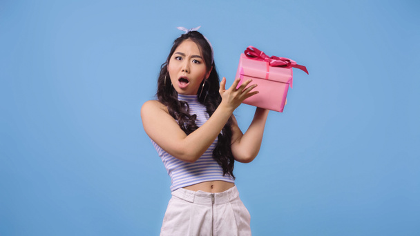shocked asian woman shaking wrapped gift box isolated on blue  - Photo, Image