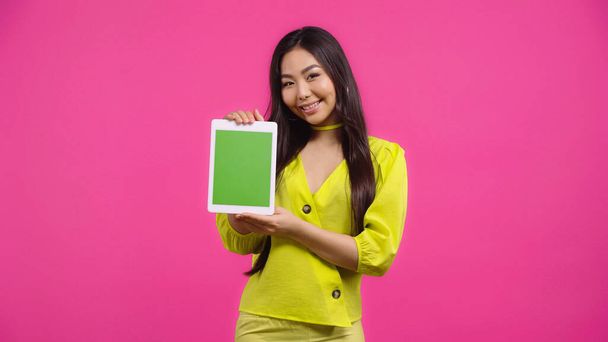 happy asian woman holding digital tablet with green screen isolated on pink   - Foto, afbeelding