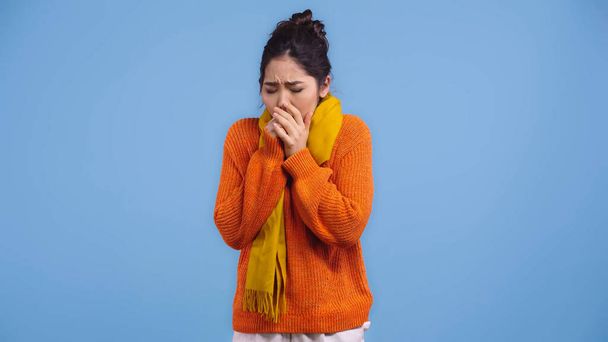 sick asian woman in orange sweater and scarf coughing isolated on blue  - Zdjęcie, obraz