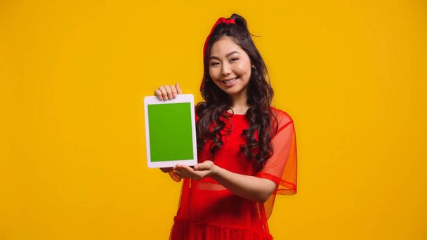 happy asian woman holding digital tablet with green screen isolated on yellow   - Фото, зображення