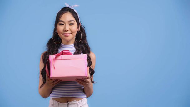 happy young asian woman holding wrapped gift box isolated on blue - Foto, Imagem