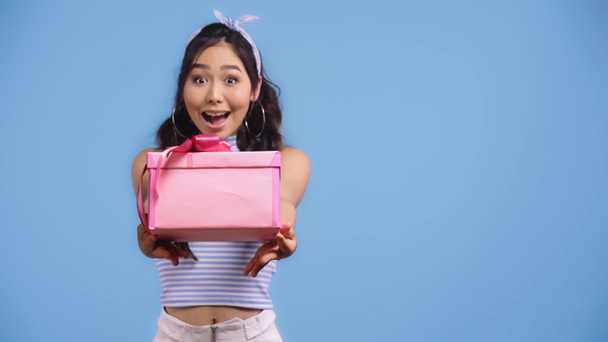 excited young asian woman holding wrapped present isolated on blue - Φωτογραφία, εικόνα