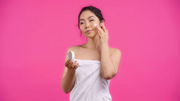 アジア系の若い女性がピンクに孤立した顔クリームを適用するタオルで  - 写真・画像