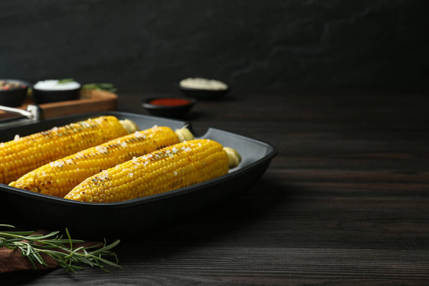 Grill pan with tasty frying corn on dark grey wooden table. Space for text - Foto, afbeelding