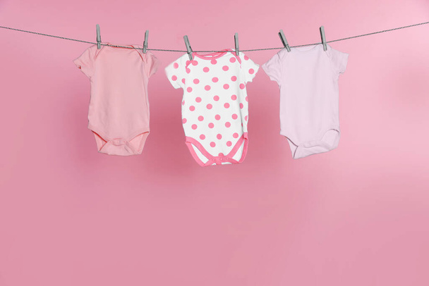 Baby onesies drying on laundry line against pink background - Foto, Imagen