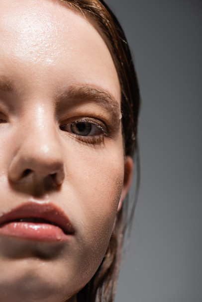 Обрізаний вид жінки з мокрою шкірою дивиться на камеру ізольовано на сірому
  - Фото, зображення