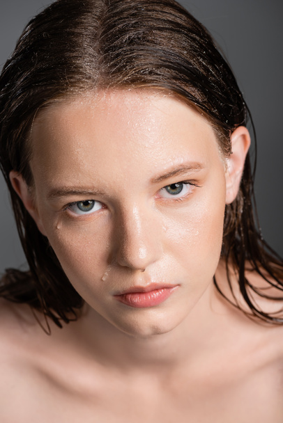 Retrato de modelo jovem com cabelo molhado e pele olhando para a câmera isolada em cinza  - Foto, Imagem