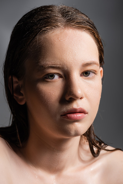 Fair haired model with naked shoulders and wet skin looking at camera isolated on grey  - Photo, Image