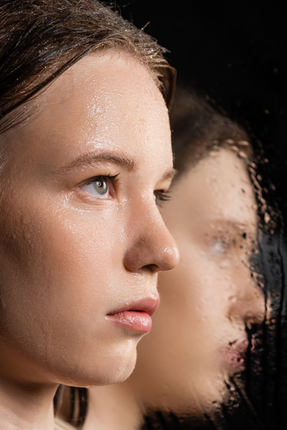 Close up view of fair haired woman with wet skin looking away near blurred mirror on black  - Photo, Image
