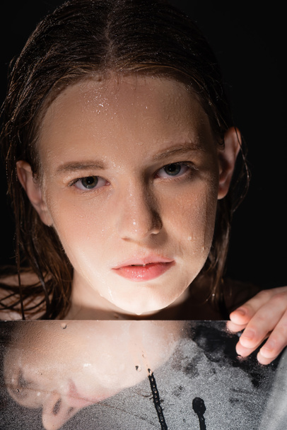 Portrait of model with wet face touching mirror isolated on black  - Photo, Image