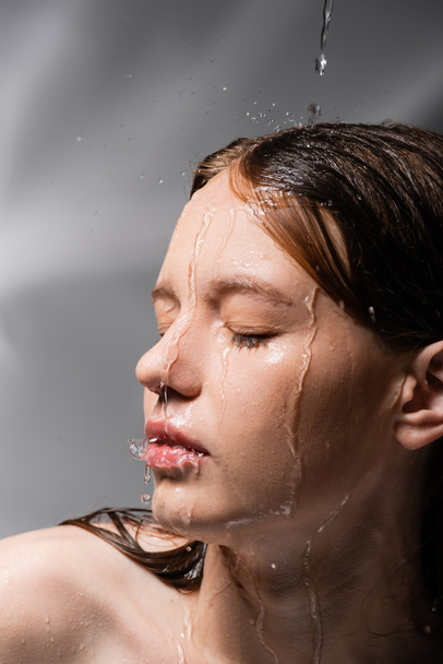 Young model with water on face and hair standing on abstract grey background  - Foto, immagini