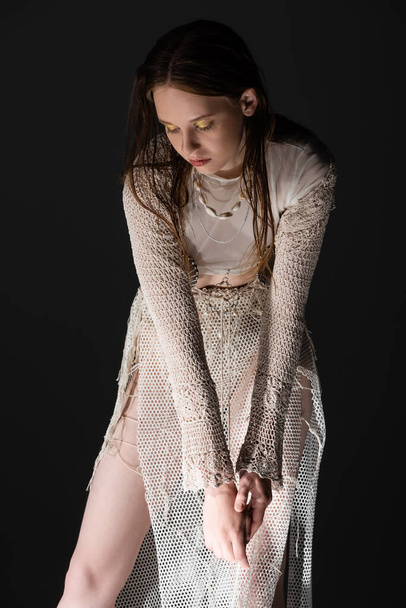 Trendy model in fishnet skirt and knitted cardigan standing isolated on black  - Photo, Image