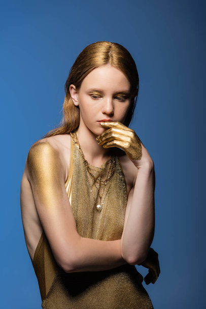 Young woman with golden paint on hands and shoulder posing isolated on blue  - Fotó, kép