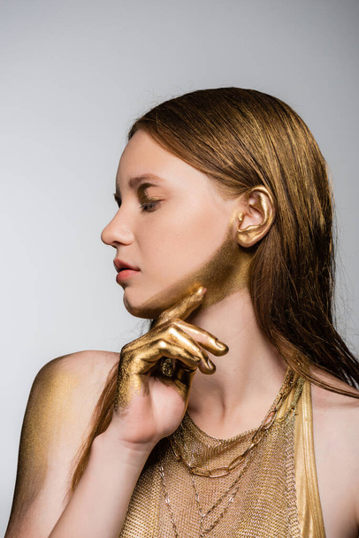 Pretty young model with golden paint on hand and chin posing isolated on grey  - Fotoğraf, Görsel