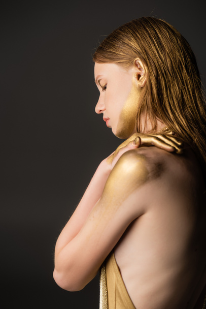 Вид збоку жінки з макіяжем і золотою фарбою на шкірі ізольовані на сірому
  - Фото, зображення
