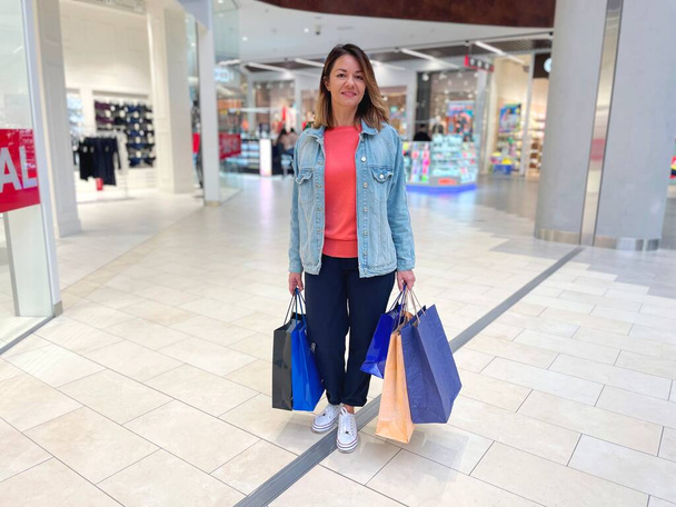 Кавказька вродлива щаслива жінка стоїть у торговому центрі, тримаючи багато сумок у руках. Весела пані витратила гроші на покупки в торговому центрі, несучи з собою покупки. Продажі сезону. Шофолік - Фото, зображення