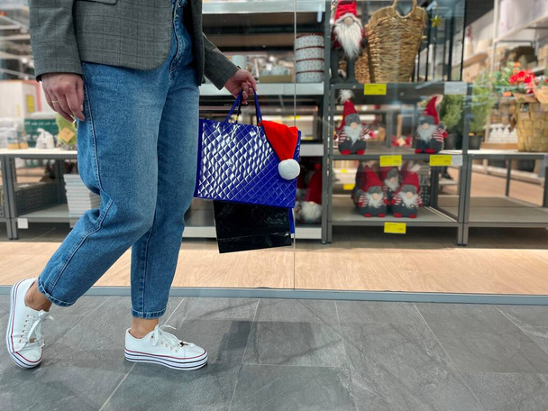 Vrouw wandelen binnen in het winkelcentrum dragen in de hand boodschappentassen met cadeautjes voor Kerstmis. Close-up van vrouwenbenen in de buurt van de winkel in het winkelcentrum tijdens de vakantie verkoop periode. Verkoop, inkoopconcept - Foto, afbeelding