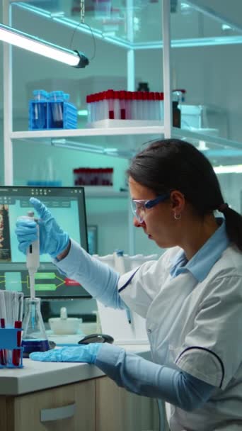 垂直ビデオ:夜遅くに設備の整った研究室で動作するチューブをテストするために液体を配管する科学者の女性。化学者は、治療開発の科学的分析のためのハイテクを使用してウイルスの進化を調べる - 映像、動画