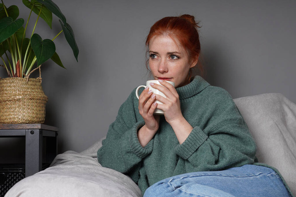 vrouw in coltrui ontspannen thuis het drinken van koffie en dagdromen - Foto, afbeelding