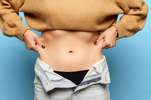 Closeup female hands stretching skin on her belly, model showing to camera her abdomen. Woman using pinch test as method for measuring body fat on belly. Concept of dieting, fitness, healthy eating - 写真・画像