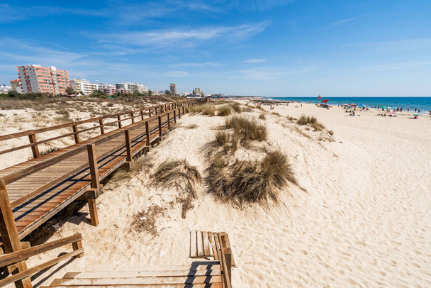Wide sandy beach with wooden bridges along the dunes in Monte Gordo, Algarve, Portugal - Photo, Image