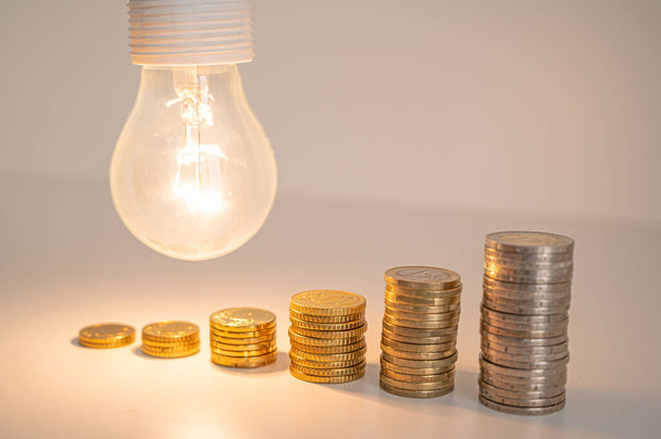 Lit žárovka s mincemi vedle sebe. Zvýšení energetických sazeb. Účinnost a úspora energie.  - Fotografie, Obrázek