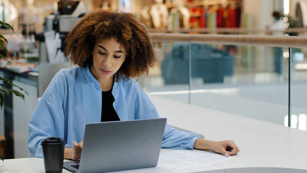 アフリカ系アメリカ人の女子学生ミレニアルビジネス女性フリーランスユーザーマネージャーカフェでテーブルに座ってコーヒーティーを飲んでノートパソコンのタイピングで作業電子ラーニング勉強ネットwifiウェブ - 写真・画像