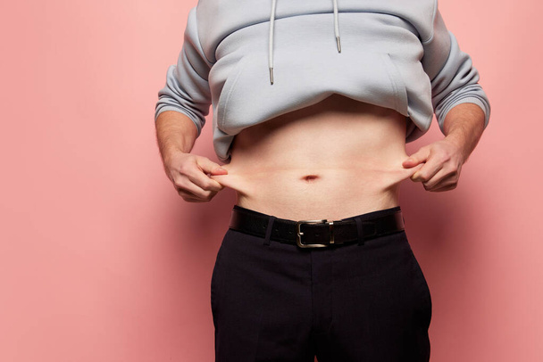 Cropped image of man showing his belly, abdomen. Close Up part of mans body. Concept of dieting, sport, fitness, healthy lifestyle, body positive. Liposuction and plastic surgery - Foto, afbeelding