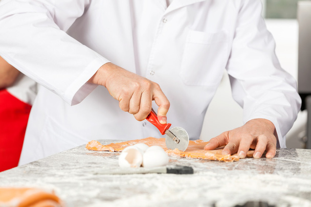 Male Chef Cutting Ravioli Pasta At Messy Counter - Фото, изображение