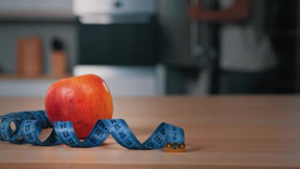 Red apple and tape measure on kitchen table unrecognizable blurred African man athlete opening fridge searching ingredients for lunch eating cooking dinner food fridge meal dieting sport nutrition - Footage, Video