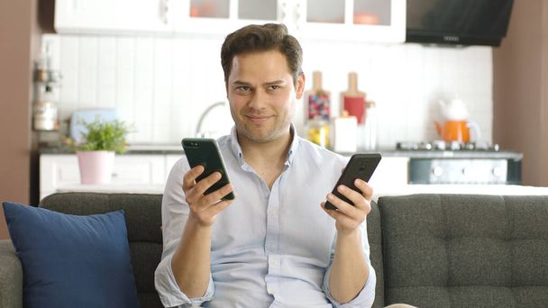 Człowiek ciężko pracuje z dwoma smartfonami w ręku starając się nadążyć za zamówieniami online patrząc na aparat zadowolony z przychodzących zamówień. Koncepcja zamawiania on-line pracowitej pracy, wykorzystanie technologii w biznesie - Zdjęcie, obraz