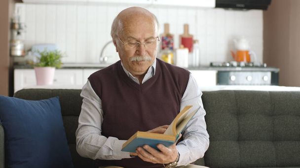 Старик читает книгу в своем мирном доме, наслаждаясь свободным временем. Счастливые пенсионеры. - Фото, изображение