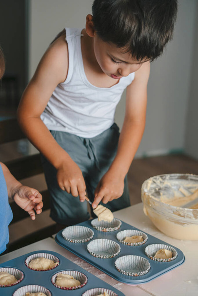 Brat i jego siostra wlewają surowe ciasto do silikonowych muffinek. Dzień Matki, rodzina, domowe pieczenie zdrowego jedzenia. Gotowanie razem, pieczenie ciasteczek - Zdjęcie, obraz