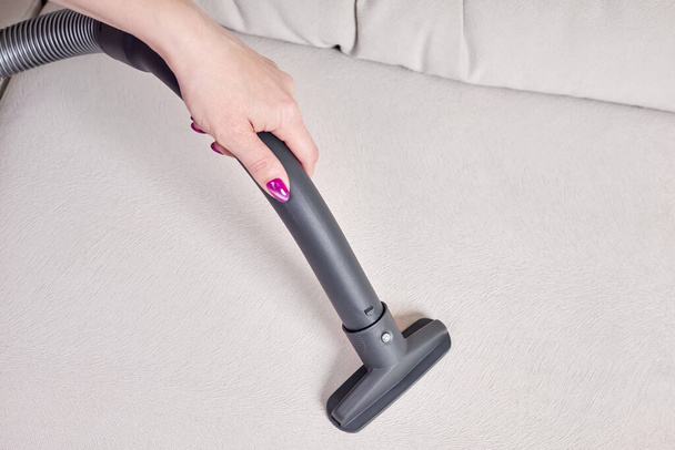 Close-up of a female hand vacuums the surface of the beige sofa - Photo, Image
