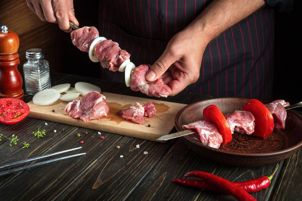 O chef amarra carne de cordeiro crua em um espeto com cebola para cozinhar carne kebab na cozinha do restaurante - Foto, Imagem