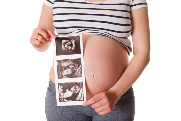 Беременная женщина стоит и держит ее ультразвуковой снимок ребенка, изолированный на белом - Фото, изображение