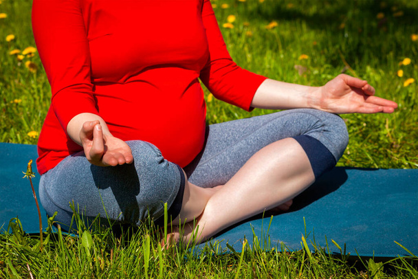 Ejercicio de yoga durante el embarazo - mujer embarazada haciendo asana Sukhasana pose de yoga fácil con mentón mudra al aire libre en césped de hierba con dientes de león en verano - Foto, imagen