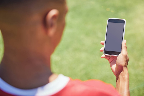 Ember, focista és telefon a pályán képernyővel, üres és mockup az interneten. Ember, focista és okostelefon a közösségi média, web vagy alkalmazás edzés, játék vagy sport pályán verseny. - Fotó, kép