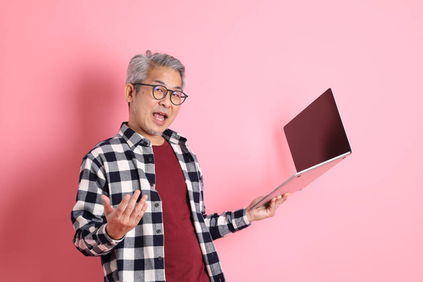 Der erwachsene asiatische Mann der vierziger Jahre stolziert mit lässiger Kleidung auf dem rosafarbenen Hintergrund herum. - Foto, Bild